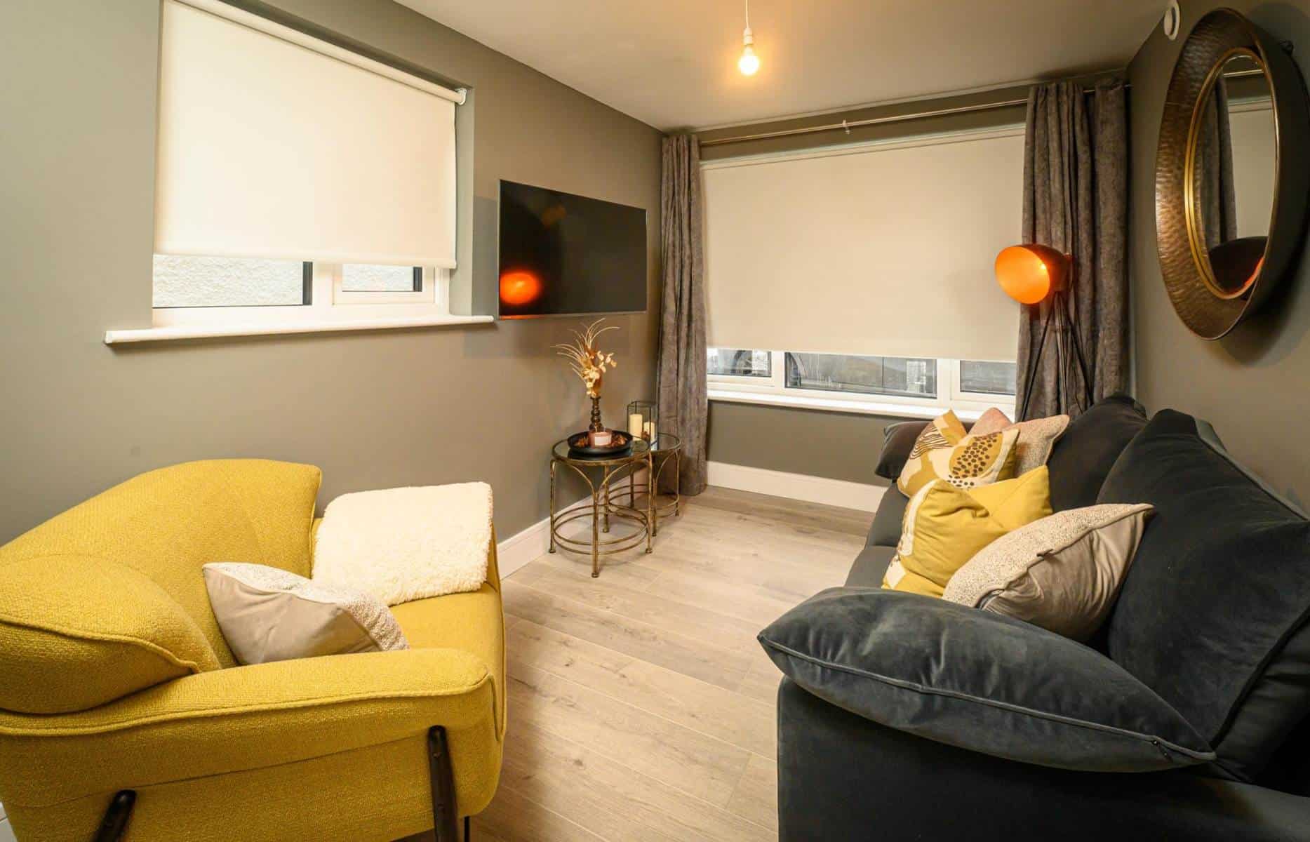 Modern living room with yellow and black sofas and large windows with blinds.